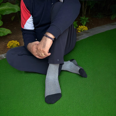 Person wearing dark pants and gray socks sitting on a green surface with plants in the background