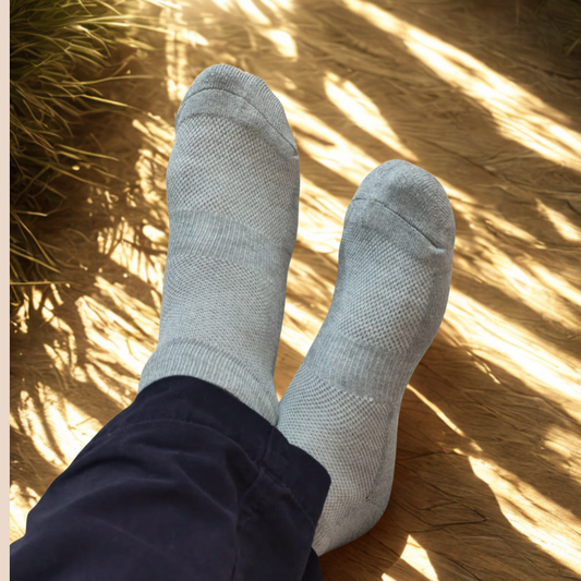 Gray socks worn with dark pants on a wooden floor with sunlight casting shadows.