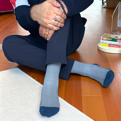 Person wearing a dark suit and blue socks sitting on a wooden floor.